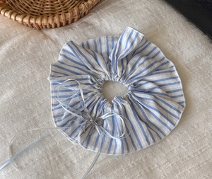 Close-up of blue striped fabric scrunchie with a silver metal bow pendant detail