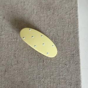 Polka dot oval hair clip in cream yellow with blue spots on textured fabric background