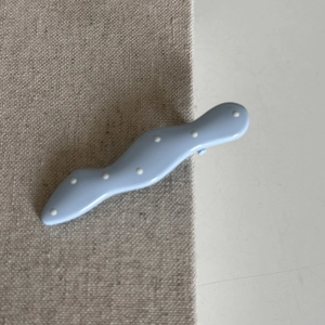 Detailed close-up of light blue wave hair clip with white polka dots on fabric