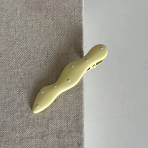 Detail showing wavy yellow hair clip with blue polka dots on a textured background