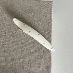 Close-up of a cream-colored hair clip featuring light blue polka dots and a metal base