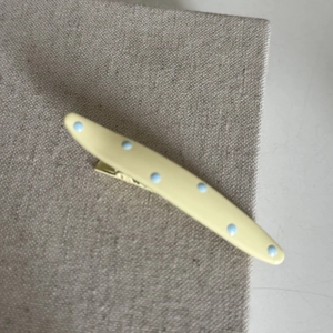 Close-up of cream yellow hair clip with blue polka dots on a textured linen background