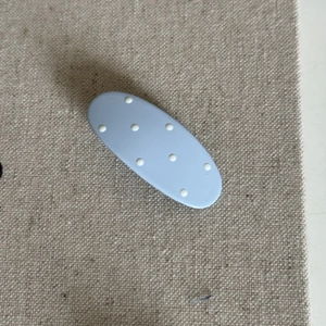 Detail view of light blue oval hair clip with white polka dots on textured linen cloth