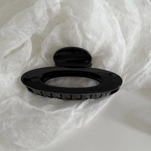 Vue détaillée de la pince à cheveux ovale noire brillante sur un tissu blanc doux