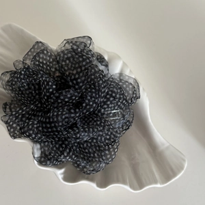 Gros plan d'une pince à cheveux fleur en résille noire à pois blancs sur plateau