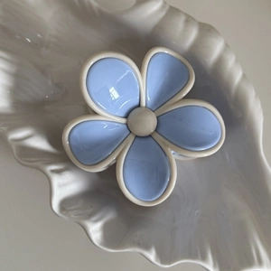 Détail d'une pince à cheveux fleur bleue et crème sur un plateau coquillage blanc