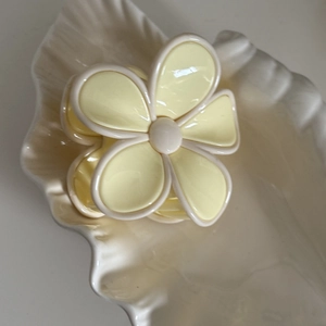 Vue détaillée d'une pince à cheveux fleur crème et jaune sur un plateau en céramique blanc