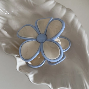 Détail de la pince à cheveux fleur crème aux bords bleus sur plateau coquillage