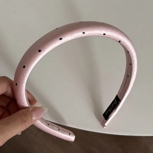 Close-up of pink padded satin headband with black polka dots and inner brand label