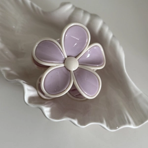 Détail d'une pince à cheveux en forme de fleur mauve et crème sur un plateau en céramique