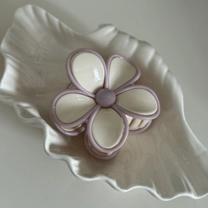 Macro d'une pince à cheveux fleur crème aux bords violets sur un plateau coquillage