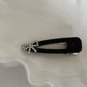 Detail shot of a black bow hair clip with sparkling white rhinestones on a ceramic tray
