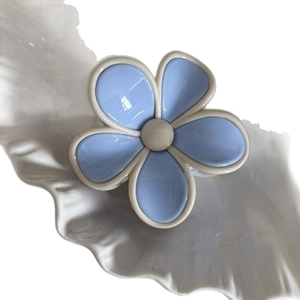 Pince à cheveux fleur bleue élégante avec touches crème sur plat décoratif blanc