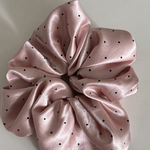 Detailed macro view of light pink polka dot satin scrunchie with silky textured folds