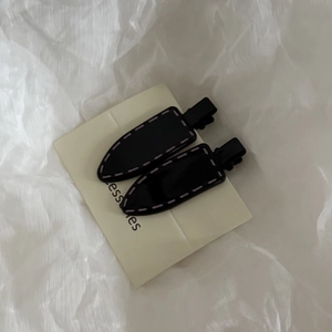 Detail of two black duckbill hair clips with pink stitching design on beige card
