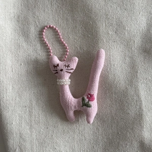 Detailed close-up of a pink fabric cat pendant with pearl necklace and embroidery
