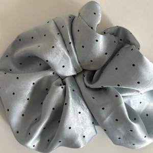 Close-up of a light blue satin scrunchie featuring a classic black polka dot pattern