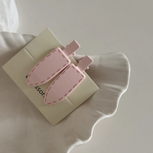 Close-up of two pink matte hair clips with stitch details on elegant display shell