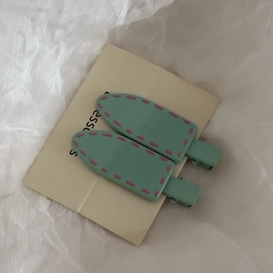Detail view of mint green hair clips with pink stitch design on white fabric