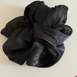 Detail shot of a black oversized scrunchie with pleated silk texture and soft satin sheen