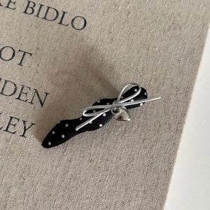 Dettaglio fermaglio per capelli a pois neri con fiocco metallico e pendente a cuore d'argento
