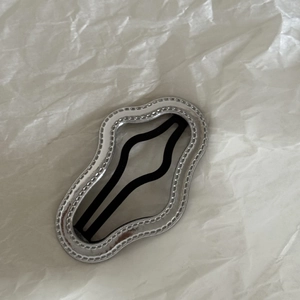Detail of silver wavy metallic hair clip with black inner part on white paper background