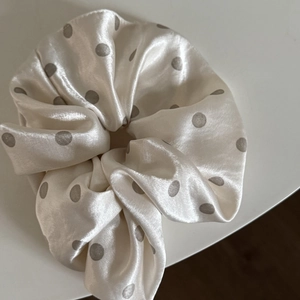 Close-up detail of smooth satin scrunchie with grey polka dots on ivory fabric