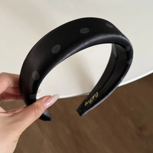 Detail of a padded satin headband with grey polka dots and a golden interior label
