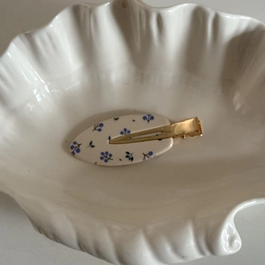 Détail d'une pince à cheveux à motif floral bleu sur un plateau blanc aux motifs de coquillage