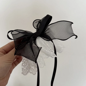 Hand holding elegant black tulle and white lace bow hairclip with long ribbon streamers