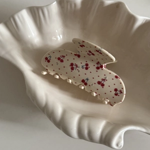 Pince à cheveux fleurie crème avec motif cerise et strass sur un plateau coquillage
