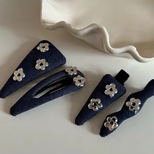 Detailed set of denim hair clips with silver flower charms on a white porcelain dish