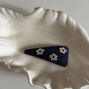 Detail of dark blue denim hair clip with silver hollow floral accents on white shell tray