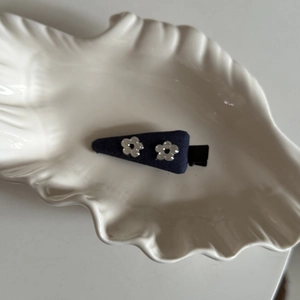 Detail of dark blue fabric hair clip with silver flower ornaments on white ceramic shell tray