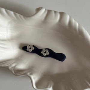 Detail of denim fabric hair clip with two silver metal flower charms in shell tray