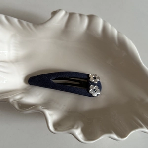 Minimalist navy denim snap hair clip with two silver metallic floral accents on shell dish