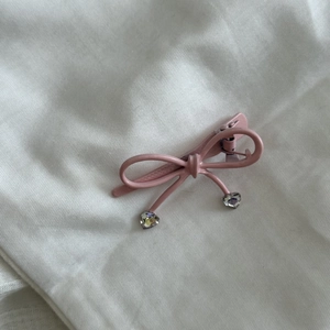 Pince à cheveux nœud rose avec pendentifs cœur en cristal sur fond de tissu blanc