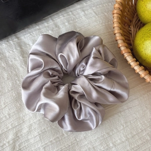 Elegant lavender satin scrunchie with silk texture shown on a white textured background