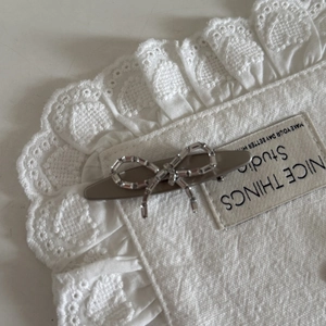 Detailed close-up of a silver zircon bow hair clip on a white lace fabric background