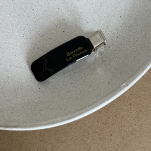 Detail view of a black acetate hair clip featuring gold La France lettering and a metal clip
