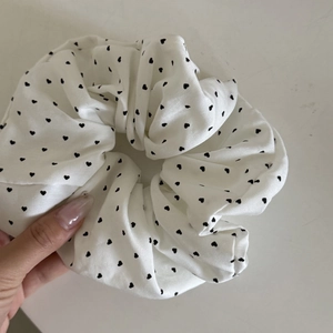 White heart print hair scrunchie with pleated fabric and elastic core in hand