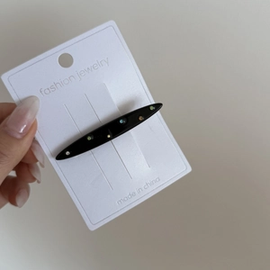 Détail d'une pince à cheveux noire avec des cristaux de couleur sur support blanc