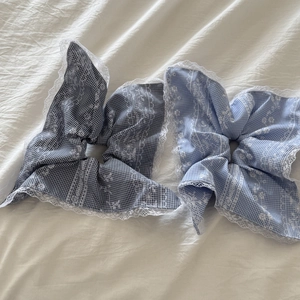 Blue plaid oversized scrunchies with white lace trim on a white fabric background