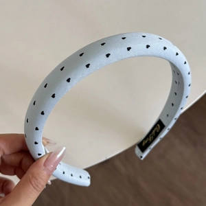 Detailed view of light blue satin headband with black heart pattern and inner brand tag