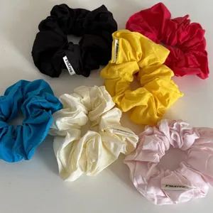 Flat lay of six colorful fabric scrunchies in black, red, yellow, and blue with brand labels