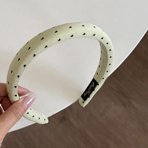 Detail of light green fabric headband featuring small black heart prints and inner label