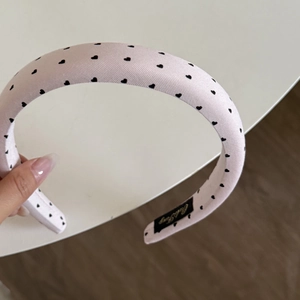 Close-up of a pink satin headband featuring black heart patterns and thick padded design