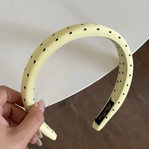 Detail of light yellow satin headband with black heart pattern held by hand