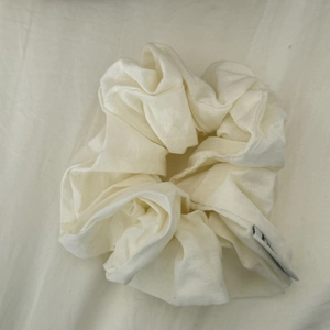 Detailed macro view of a cream cotton fabric scrunchie with a small brand label