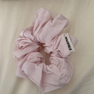 Detail of baby pink scrunchie with soft fabric texture and stitched brand label